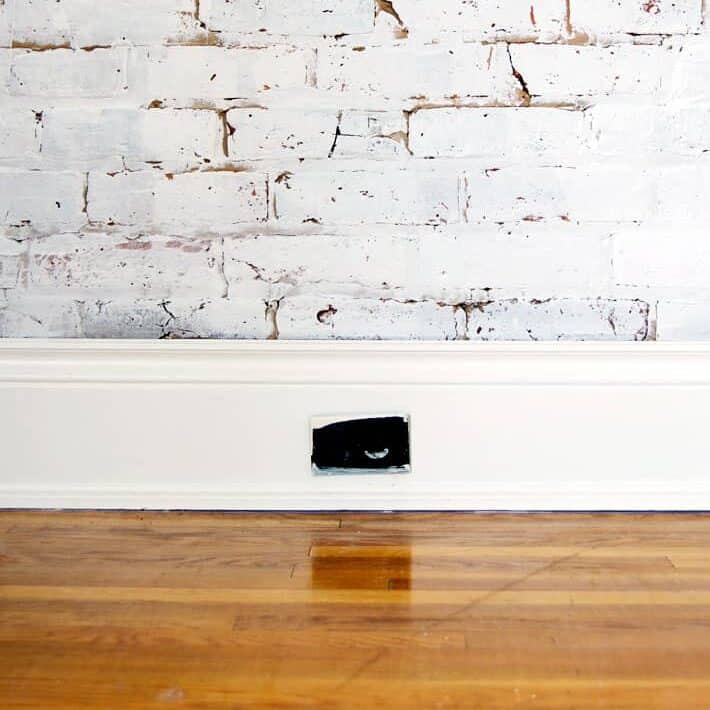 Old, ugly electrical outlets? Replace them. Here's the how-to guide ... White brick wall with wide white baseboard, dark brown, paint splattered old electrical outlet in the middle of the baseboard.