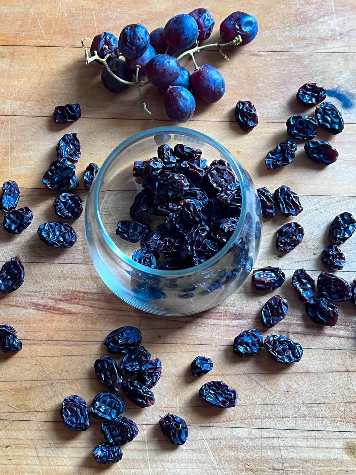 Homemade raisins in a glass jar with purple grapes behind.