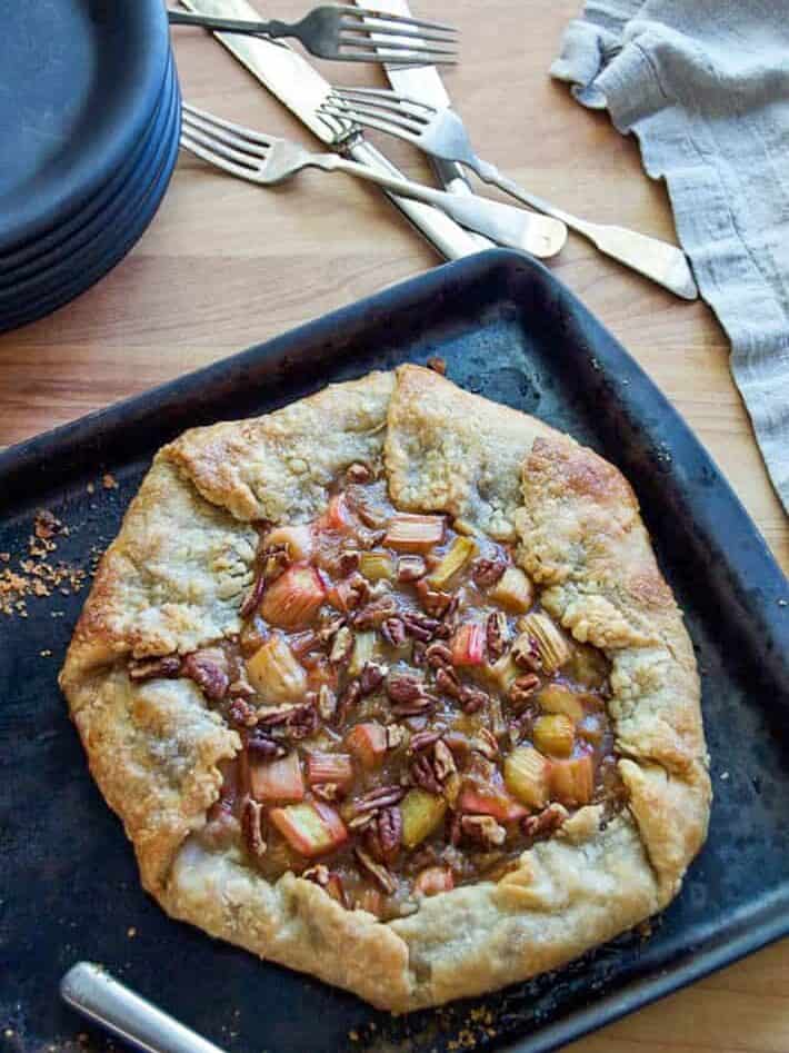 Bubbling rhubarb tart on a dark baking pan with silverware scattered about.