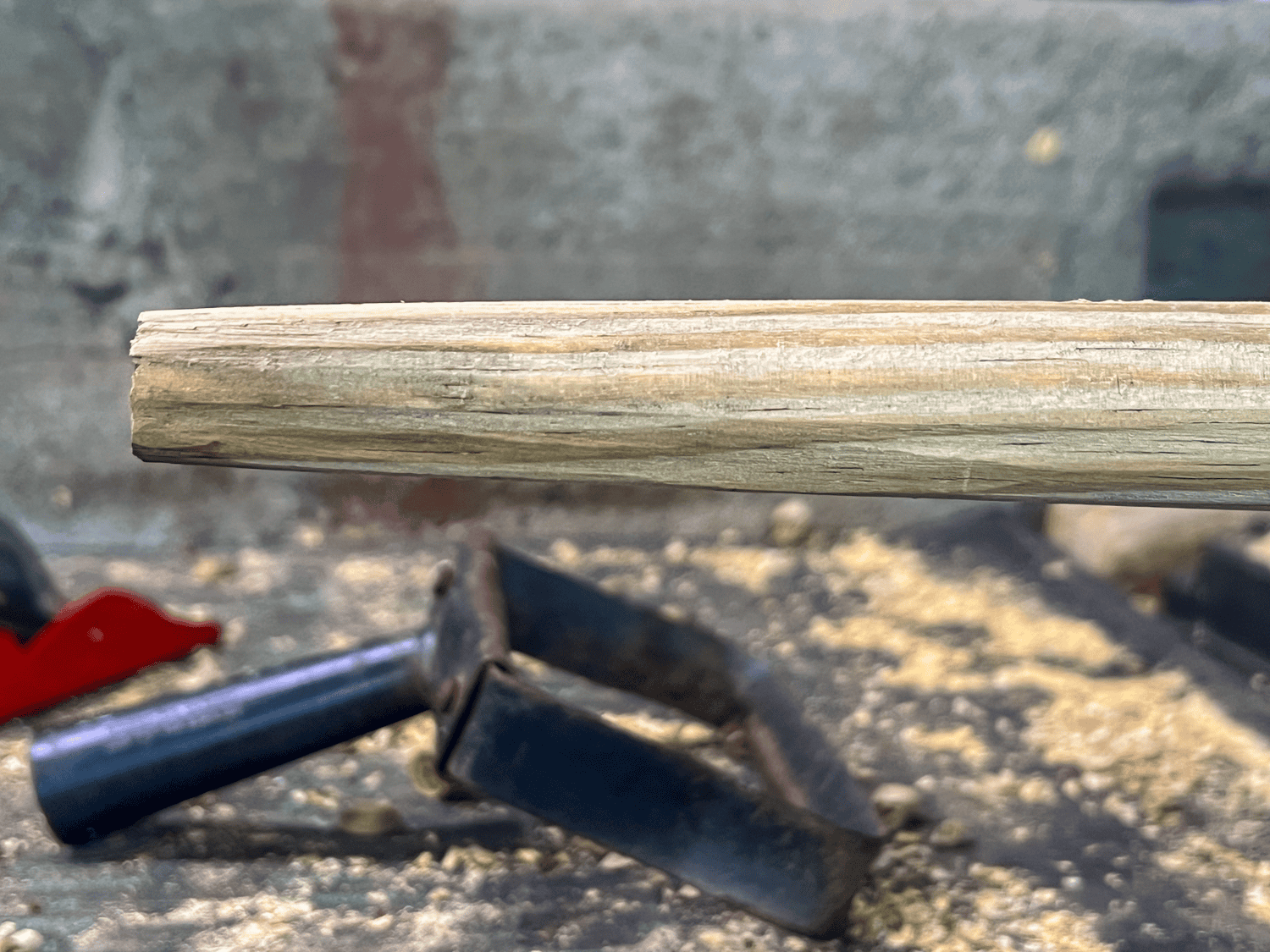 An old wood tool handle, planed by hand with shavings and shuffle hoe head underneath.