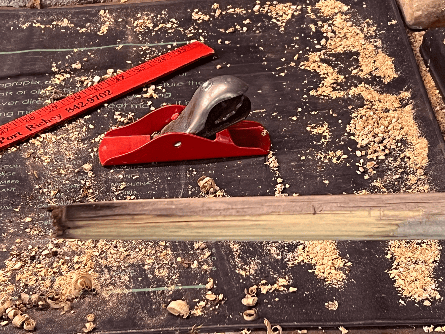 Broken shovel handle with jagged and discoloured end, a red hand planer, yardstick and wood shavings below.