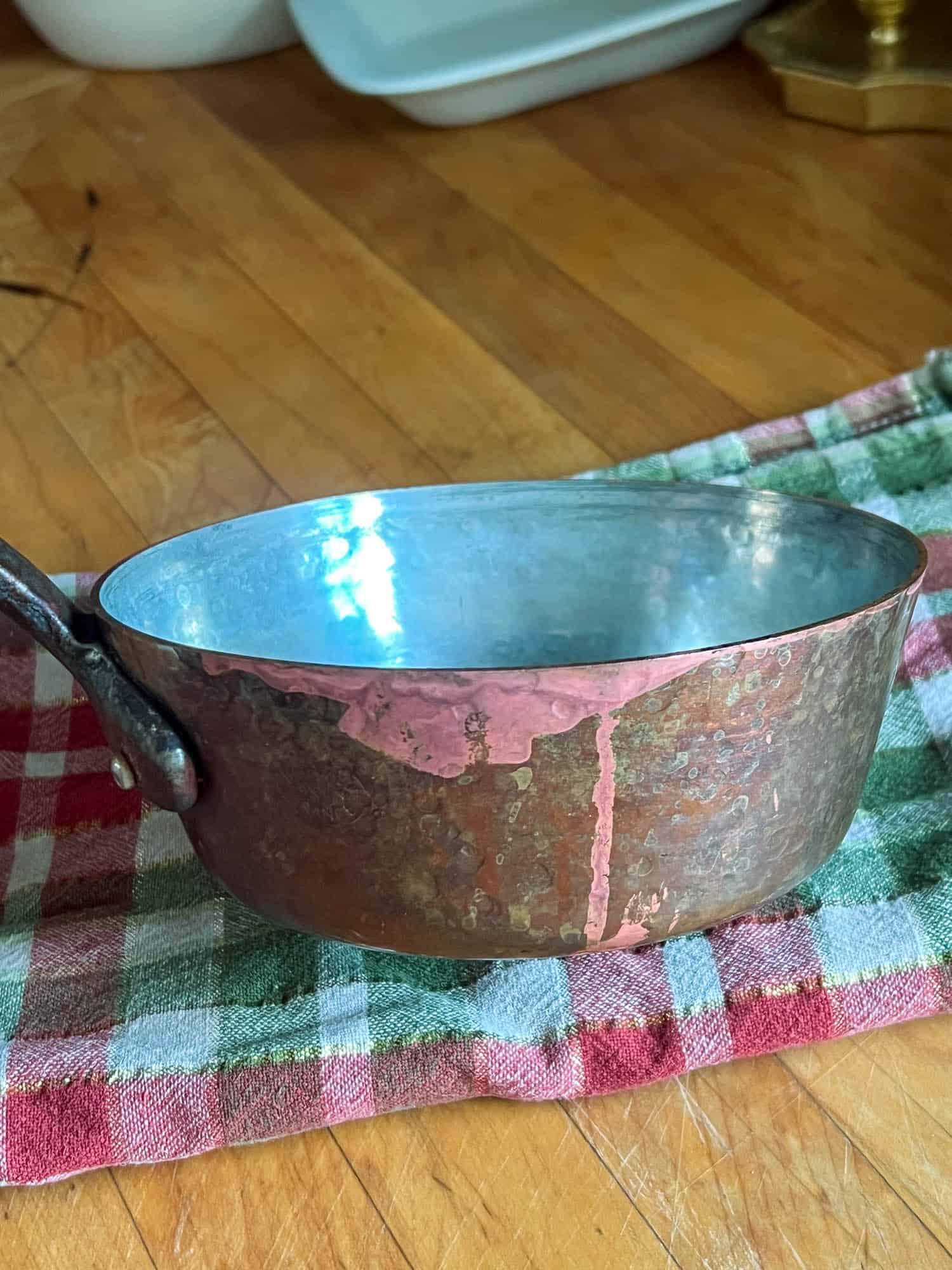 A copper pot showing bright clean spots where something acidic dripped down the side.