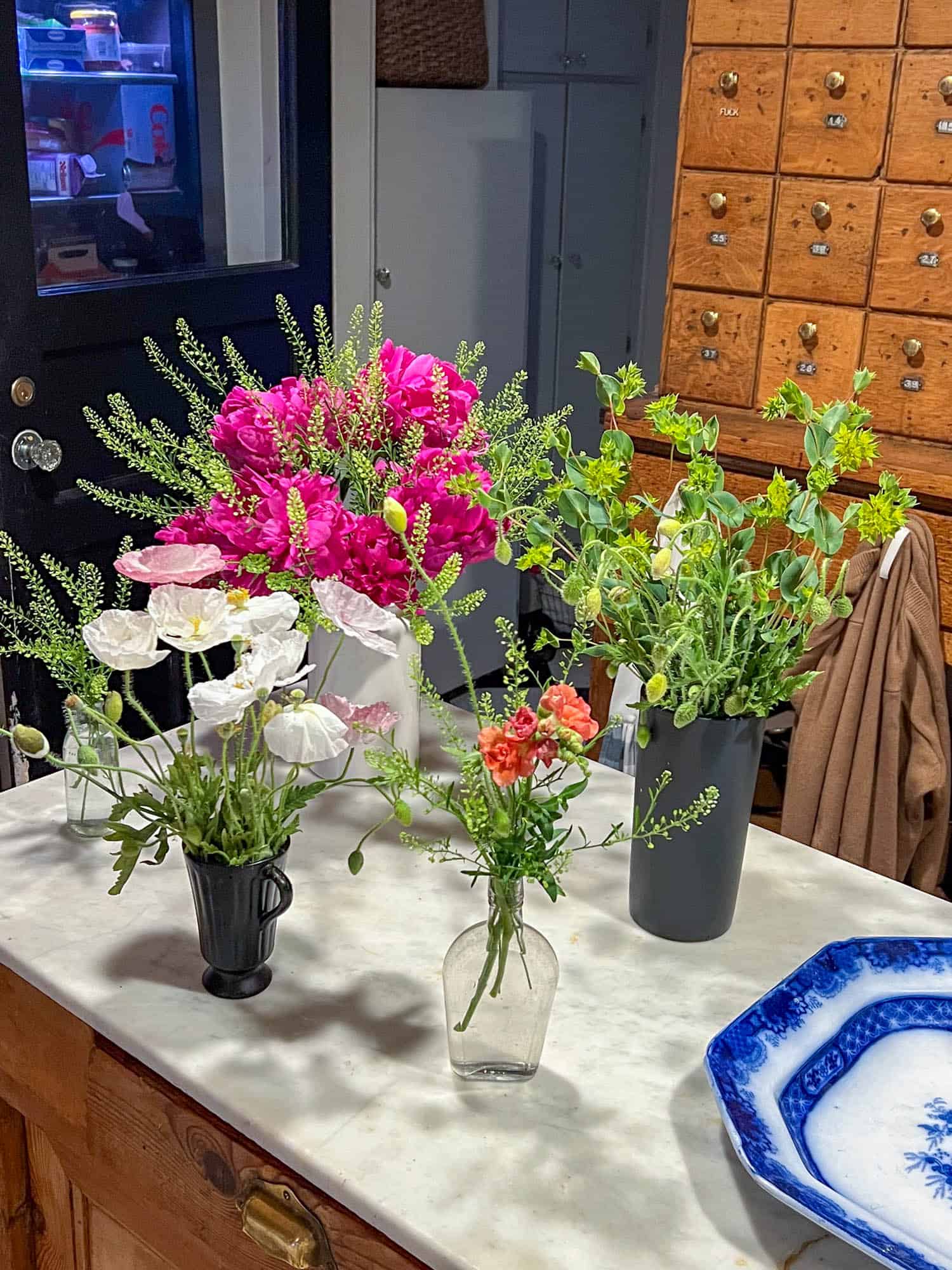 A. marble tape with black, clear and white vases filled with pastel poppies, bright pink peony, and lime green cress and bupleurum.