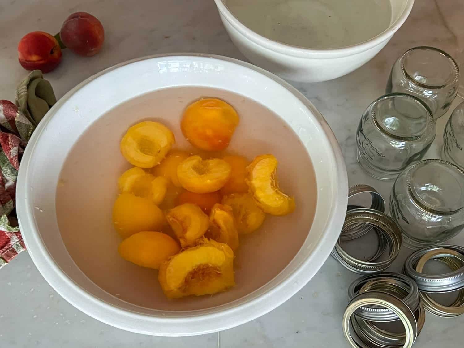 Sliced, peeled peaches sit in an ironstone bowl filled with anti-browning solution.