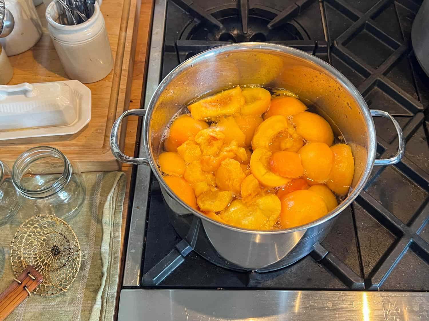 Prepped peaches for canning sit in a simple syrup to heat up on a stove.