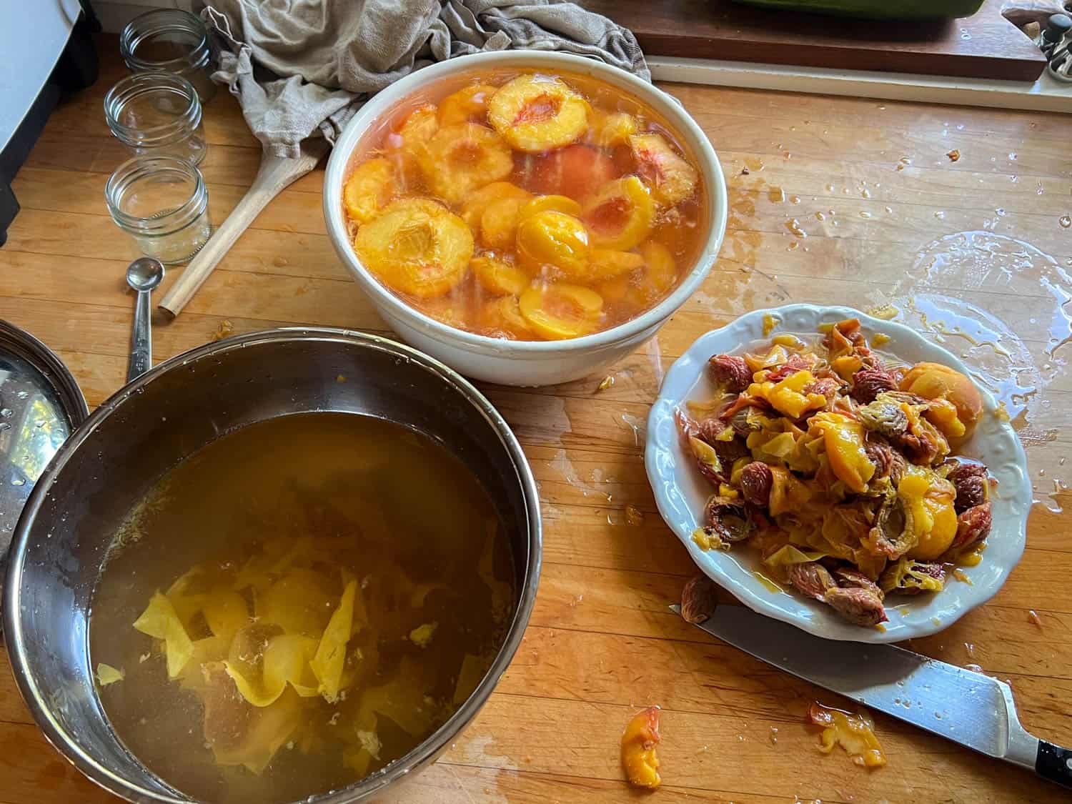 A sticky, messy wood countertop with bowls and pots filled with peaches, peach juice, peach pits.