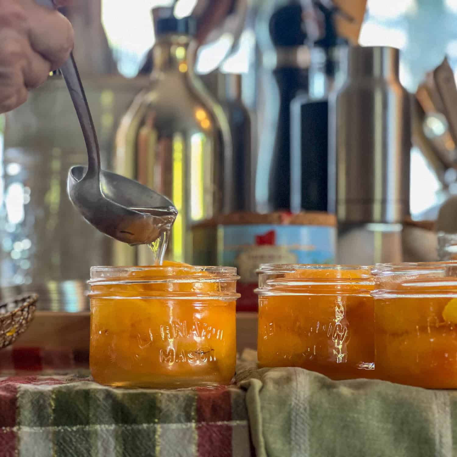 Ladling simple syrup into a 250ml mason jar filled with peaches.