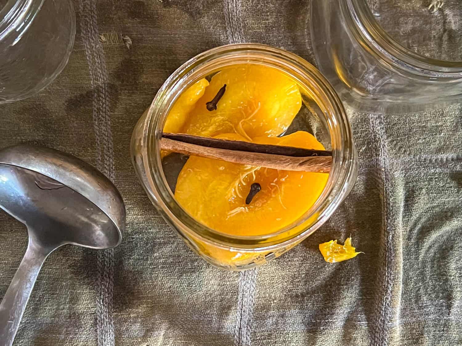 A cinnamon stick across a mason jar with shoulders holds peach slices down for canning.