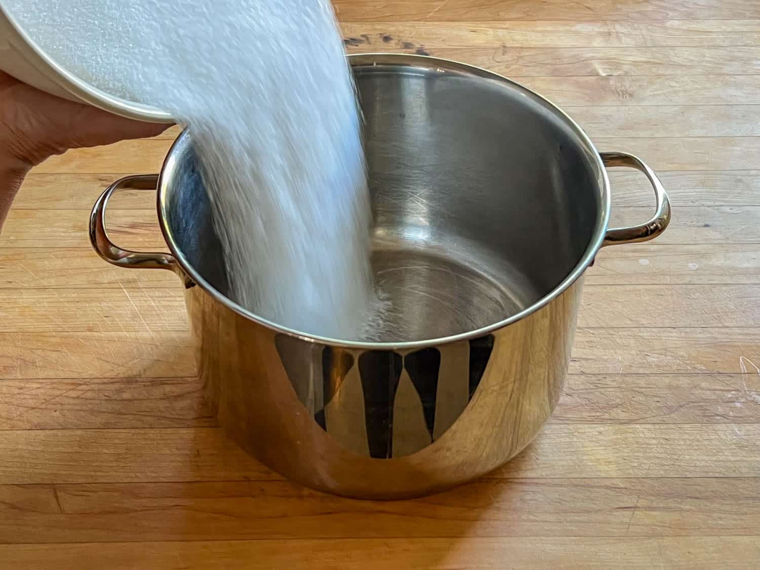 6 cups of sugar being poured out of bowl into large pot.