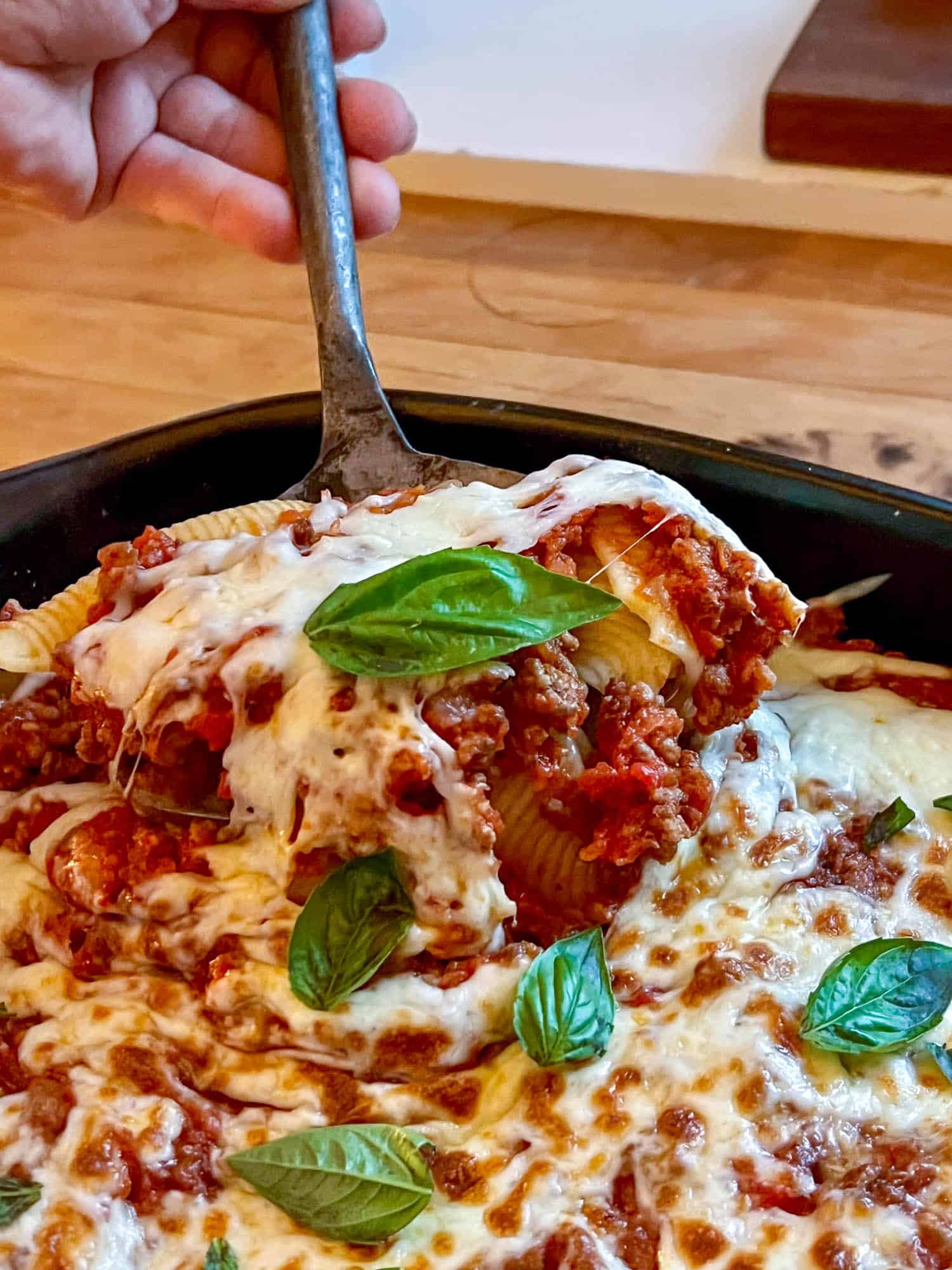 Pasta shells with meat sauce, mozzarella cheese, and fresh green basil leaves.
