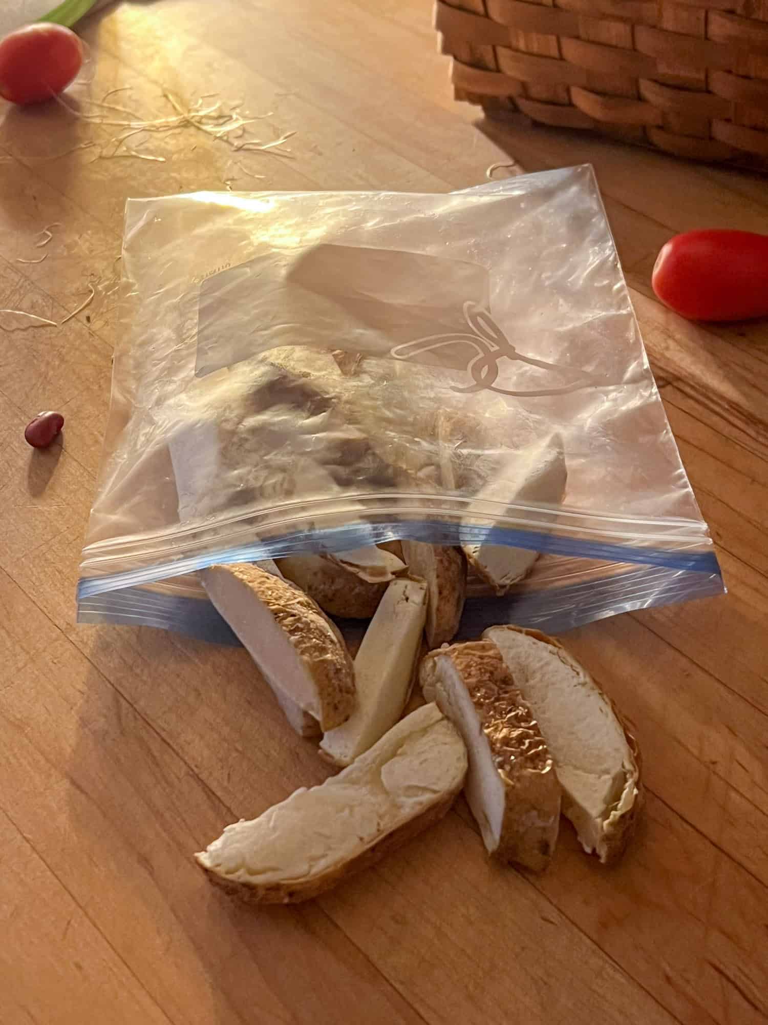 Baked potatoes cut into fry slices being held in a freezer bag before cooking.