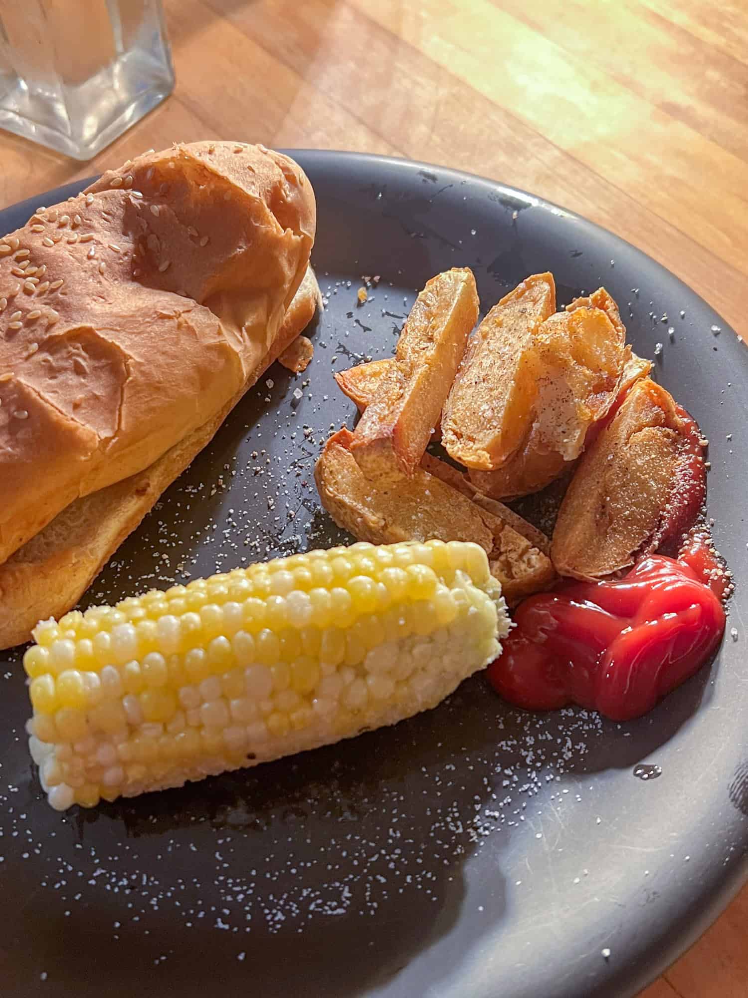 Thick cut french fries with a crispy exterior beside a hot dog and half a cob of corn on a plate.