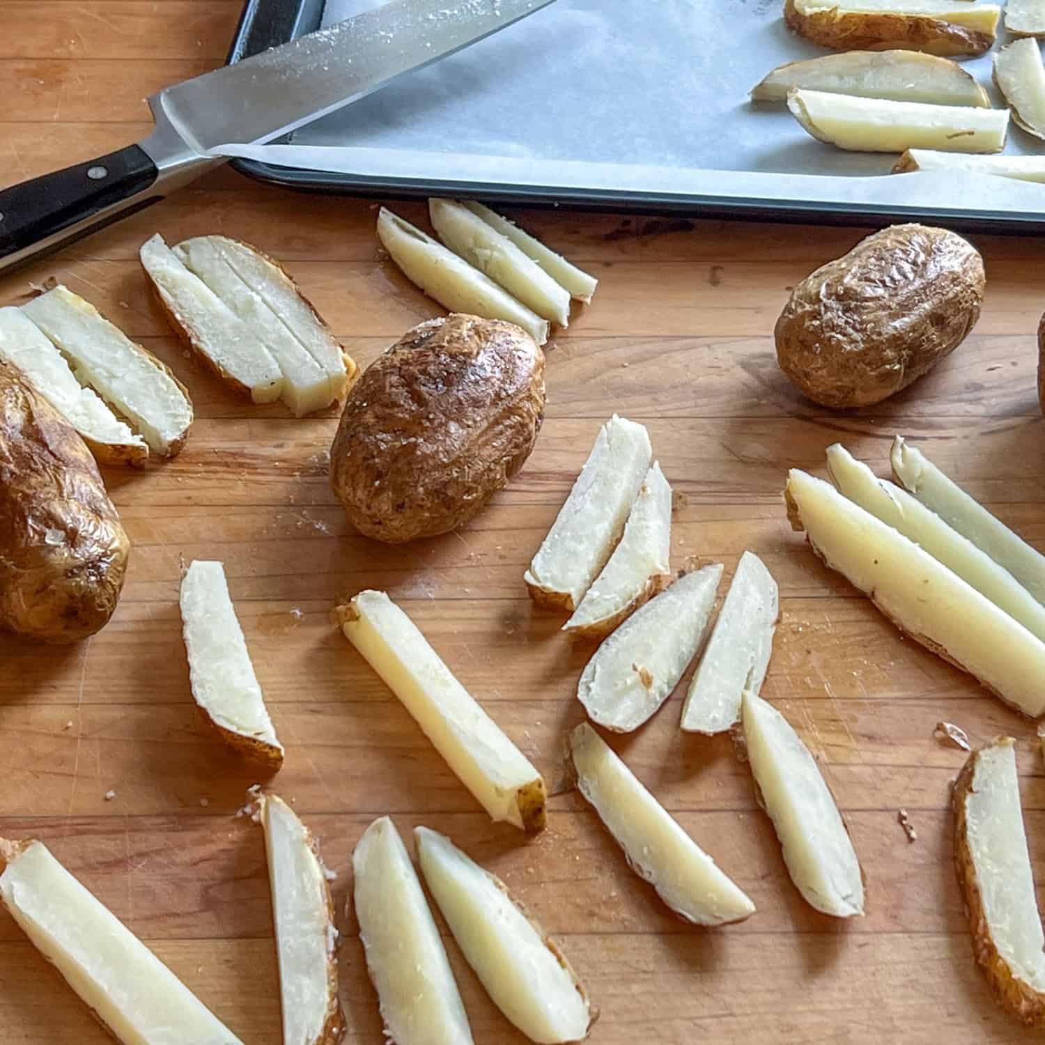 Baked potatoes laying amongst fries cut out of baked potatoes on a wood countertop.