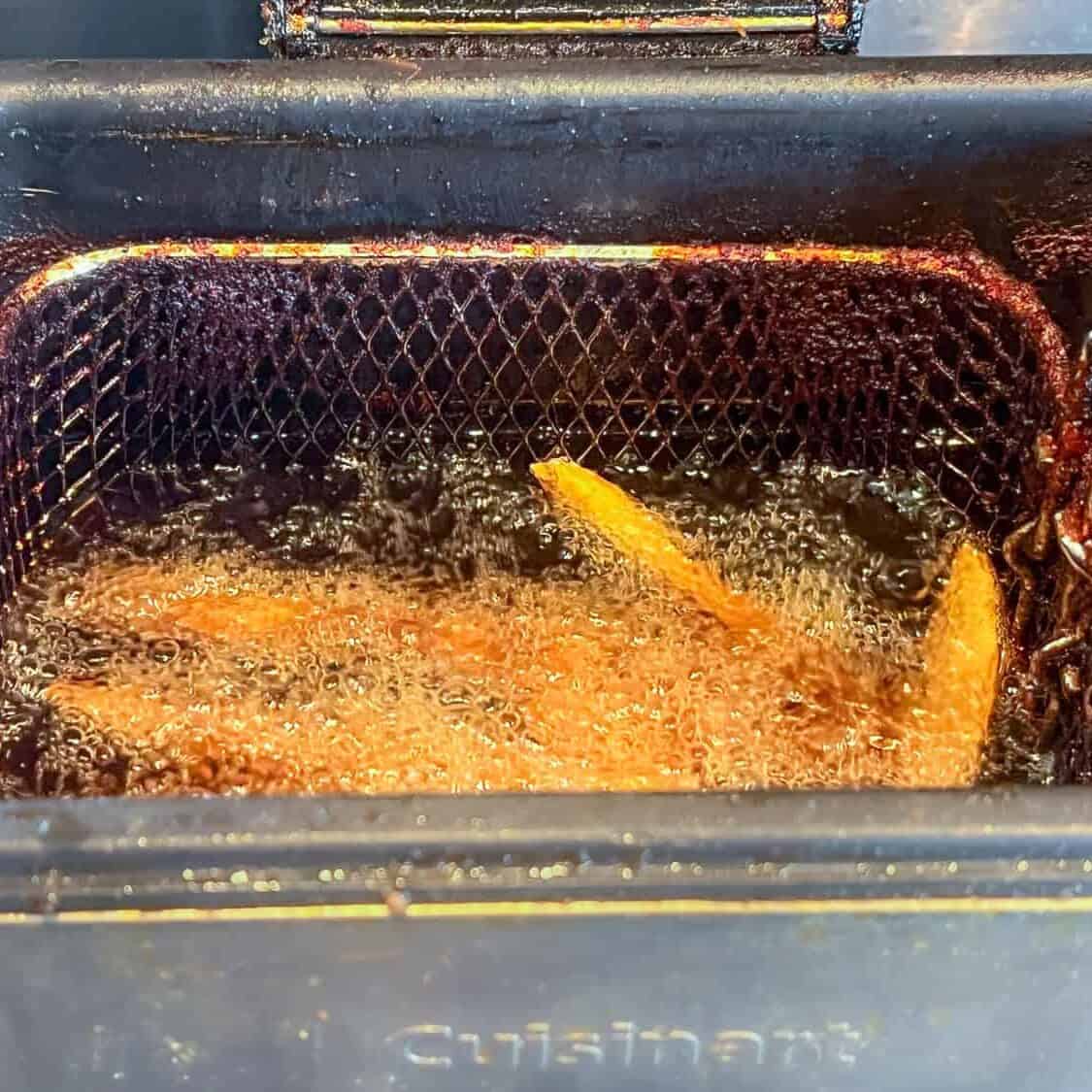 Baked potato fries bubbling in the oil of a Cuisinart deep fryer.