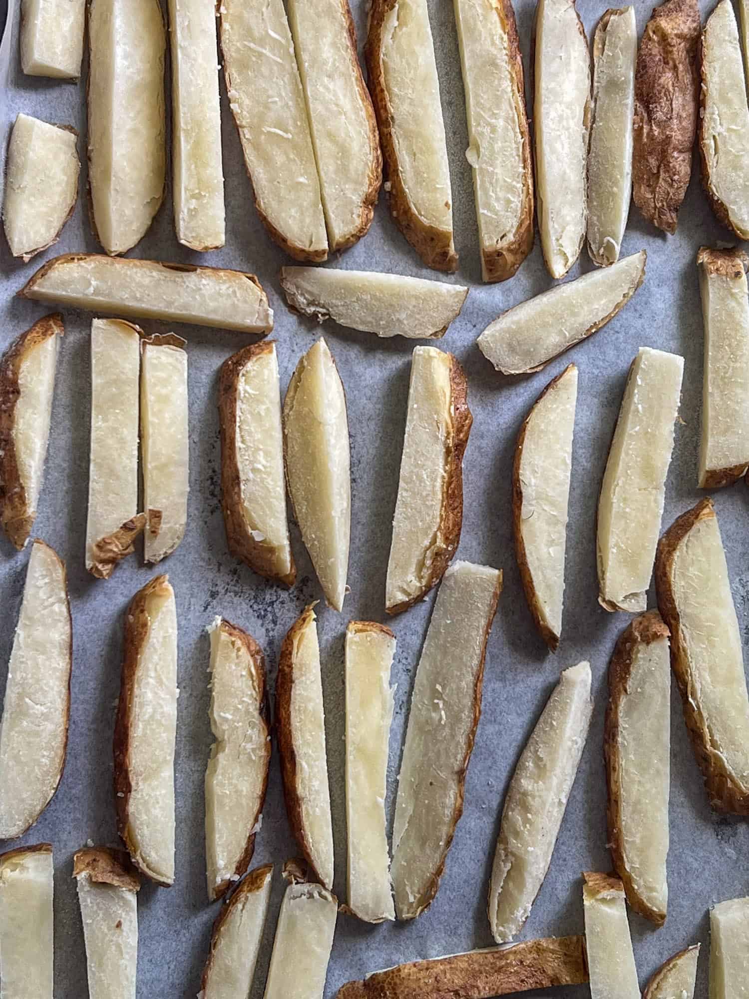 Baked potatoes cut into fry shapes laid on parchment paper for freezing.