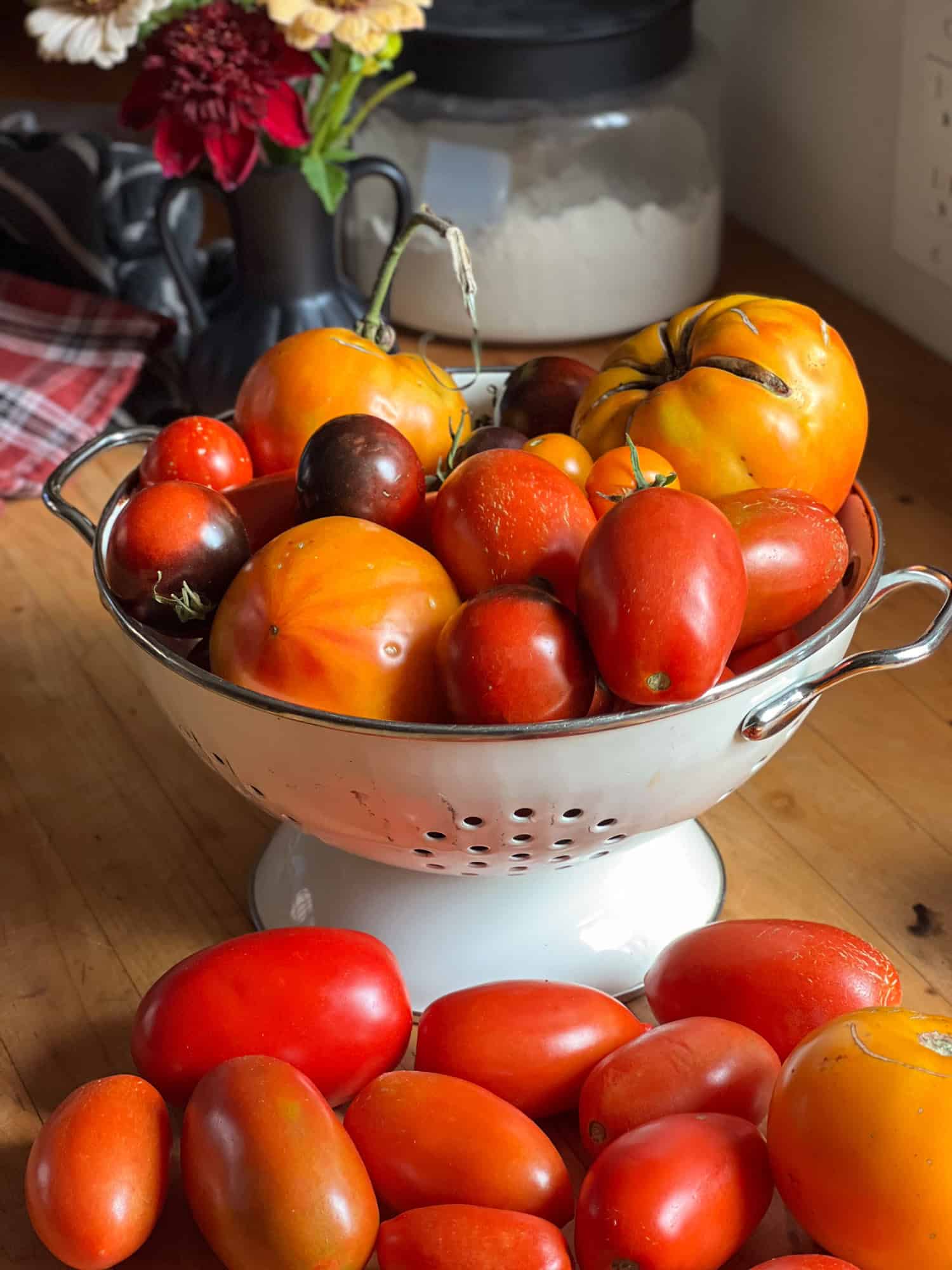 Heirloom tomatoes fill a white enamel colander on a butcher block countertop.