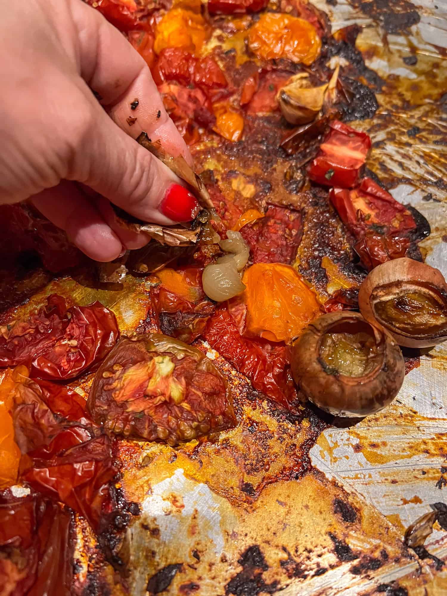 A woman's hand squeezes a clove of roasted garlic out of its peel.