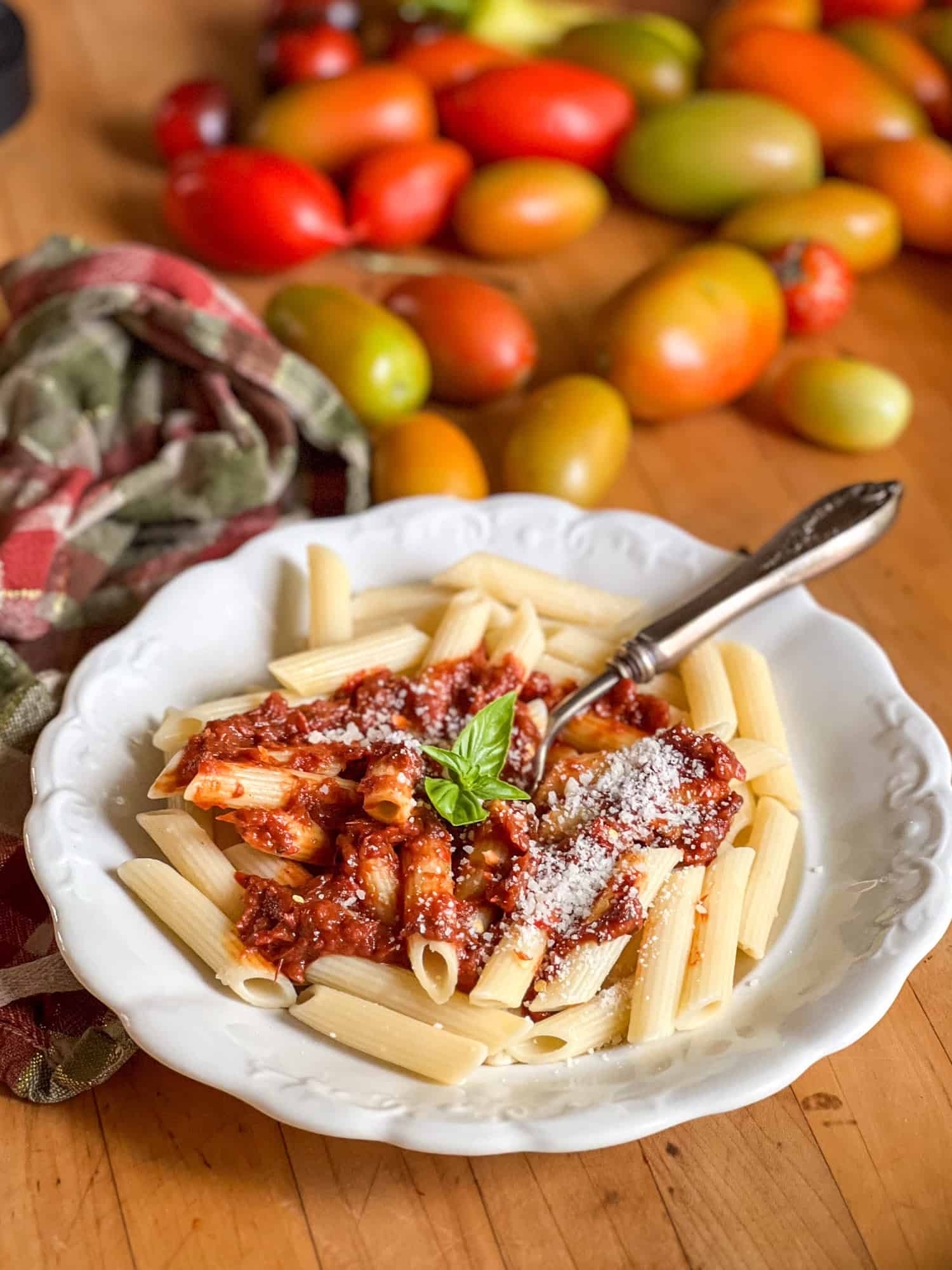 Penne pasta in an ironstone bowl with a sprig of basil and roasted tomato sauce on it