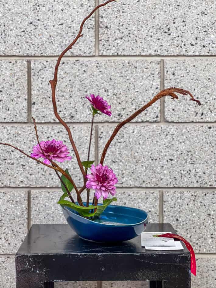 Purple dahlias, sticks and greenery in a blue vessel.
