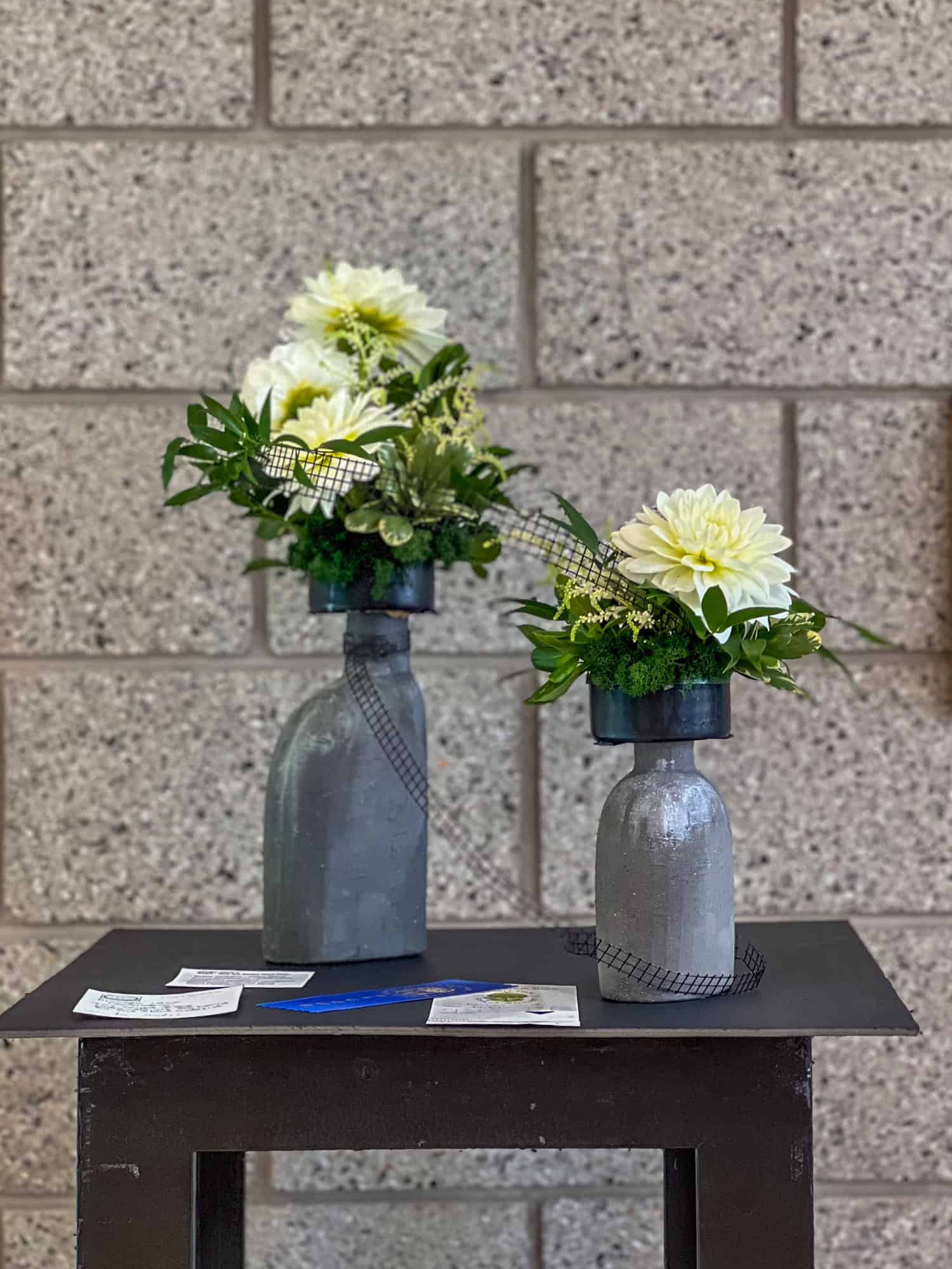 Exhibition flower arrangement of white dahlias and greenery in 2 organic modern grey vases.
