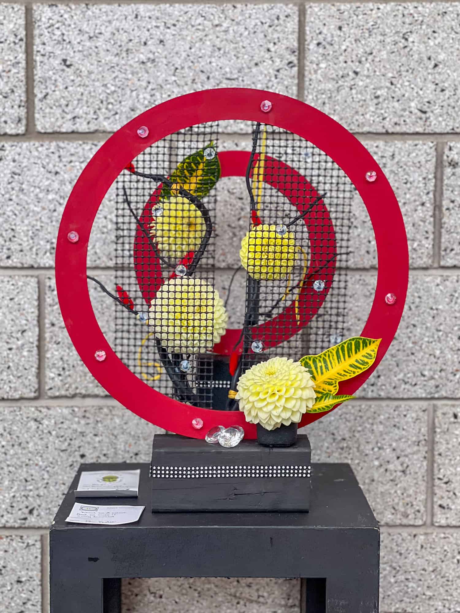 An exhibition floral design with creamy white dahlias and red circular structures.