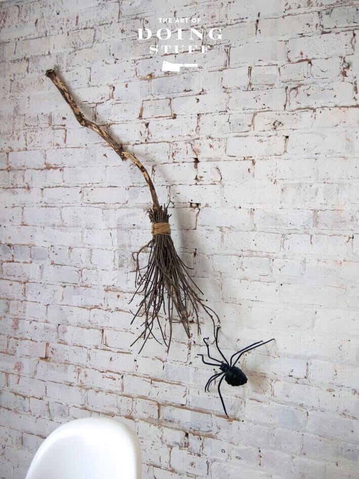 Witch's broom hanging on brick wall aside a huge spider.